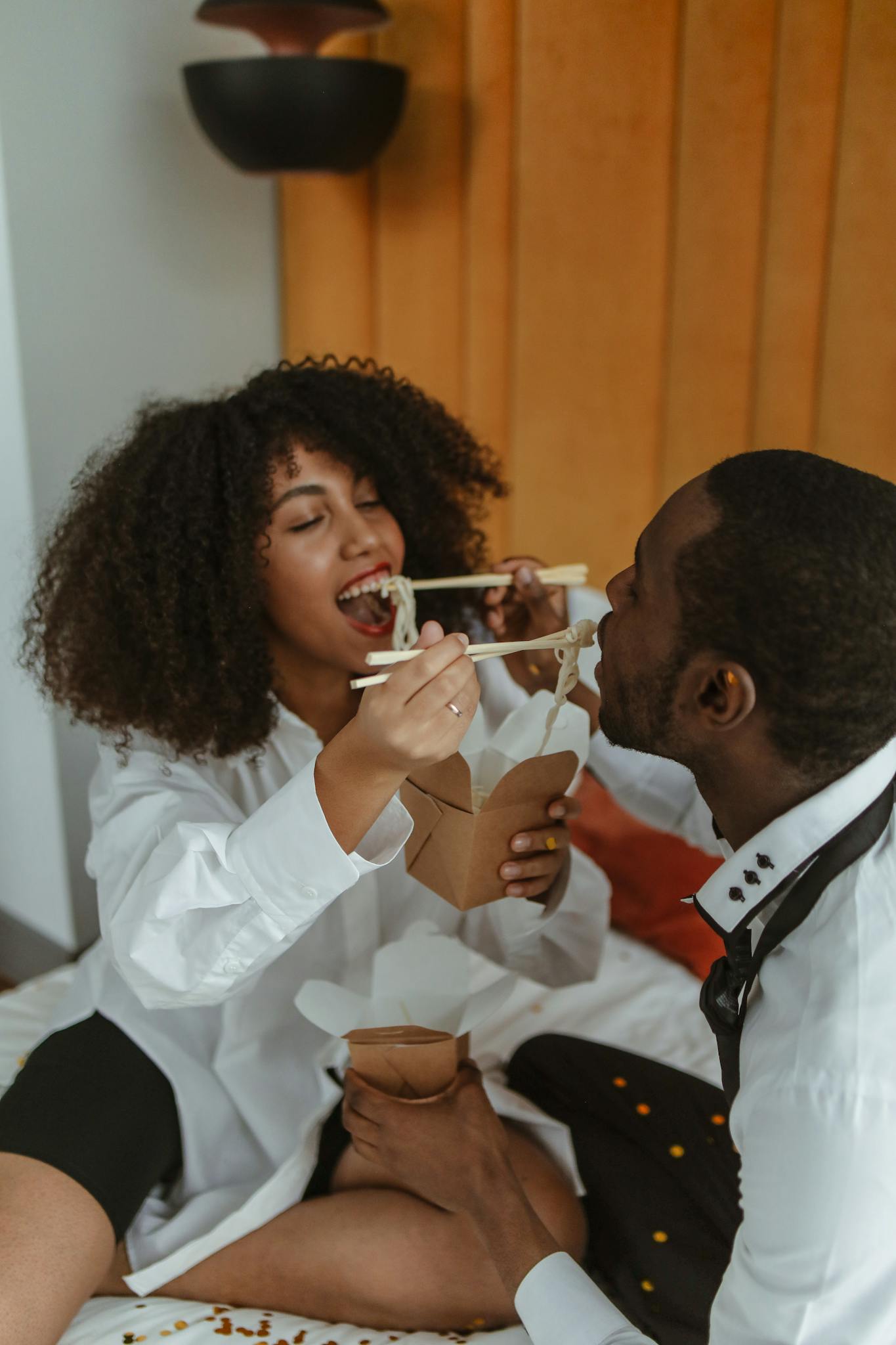 African American couple sharing a meal with chopsticks on a cozy bed.
