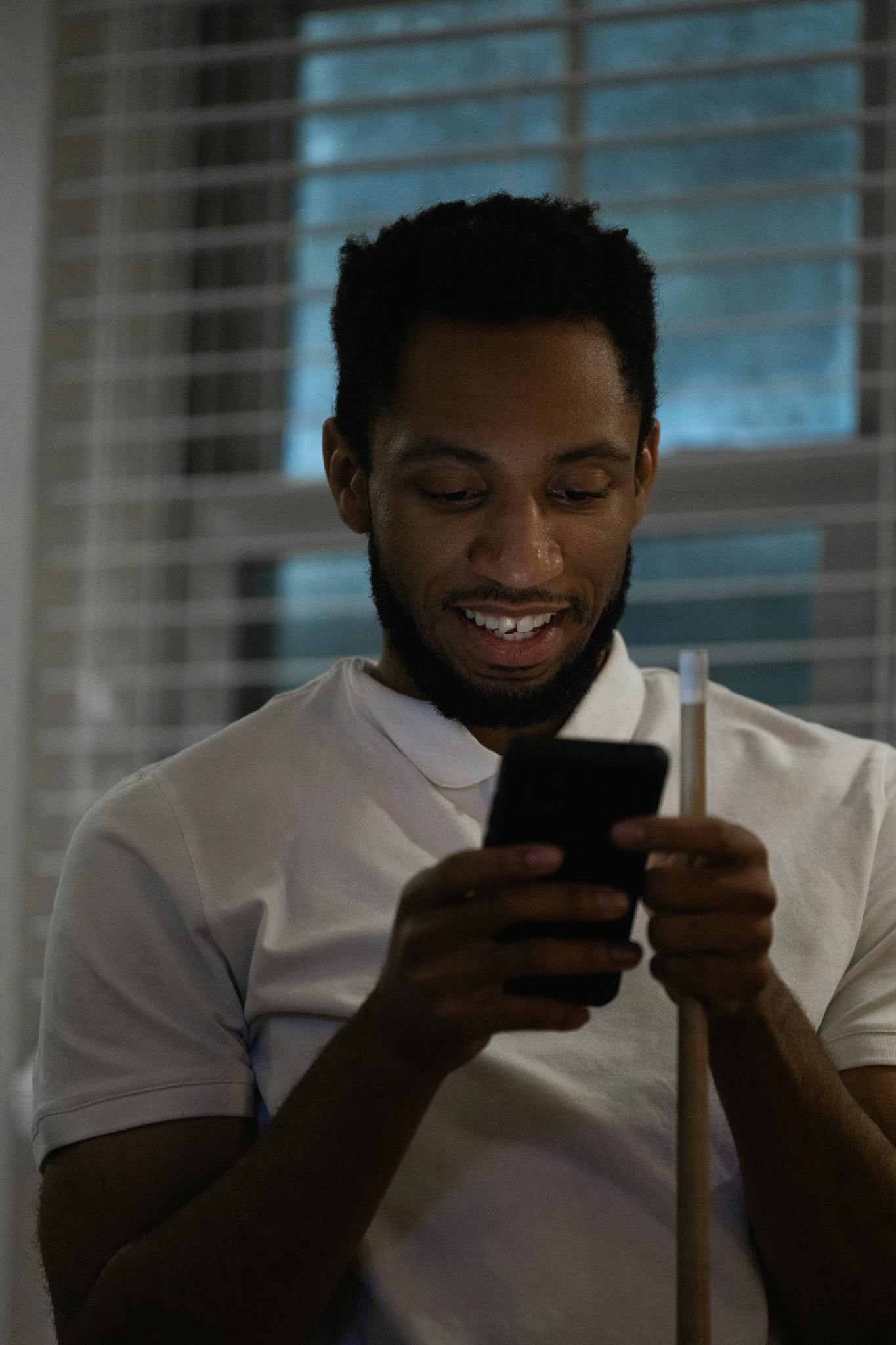 African American man in a white polo shirt using a smartphone indoors, smiling at a message.