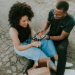 Happy couple sitting on the pavement enjoying sushi from a paper bag outdoors.