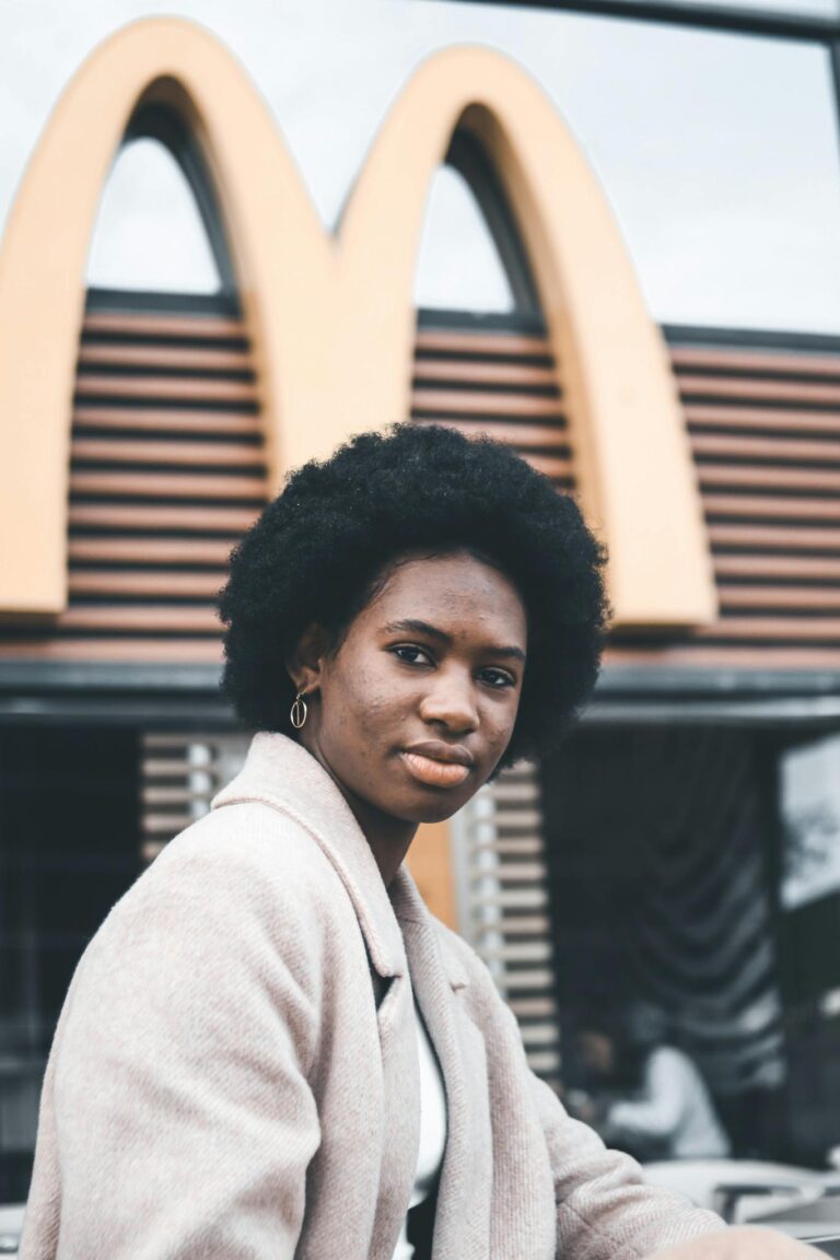 Portrait of a woman with afro hair sitting outside a fast food restaurant, showcasing style and confidence.