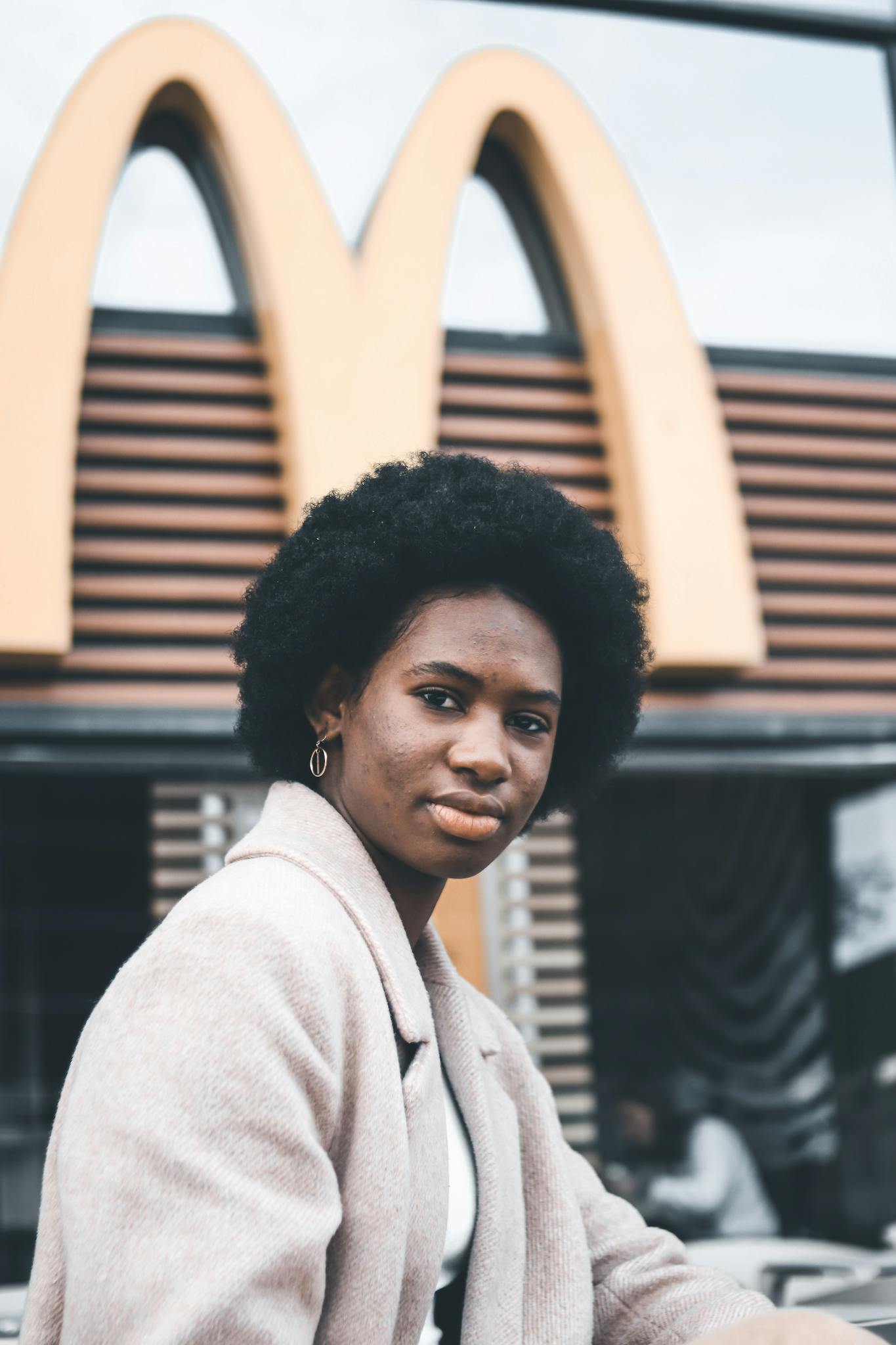 Portrait of a woman with afro hair sitting outside a fast food restaurant, showcasing style and confidence.