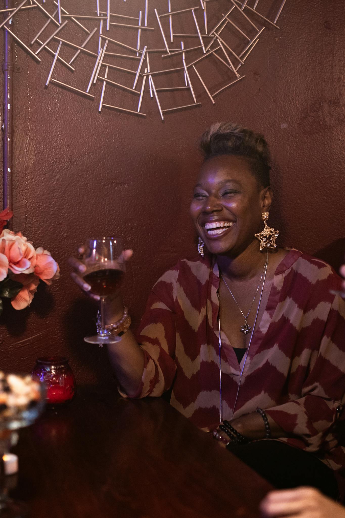 Smiling woman enjoys a glass of wine in a cozy, dimly lit setting, creating a warm atmosphere.